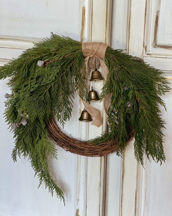 Corona navideña artesanal con ramas naturales, tuya fresca y campanitas metálicas