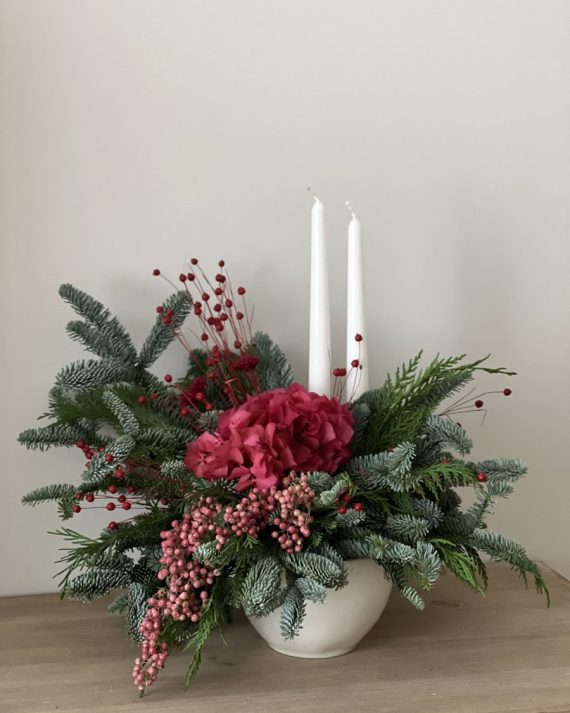 Centro navideño con dos velas blancas, hortensia preservada fucsia y abeto fresco