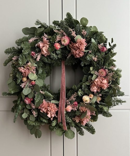 Corona de Navidad rosada con abeto y flor seca, colgada como decoración