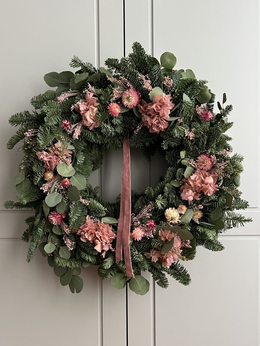 Corona de Navidad rosada con abeto y flor seca, colgada como decoración