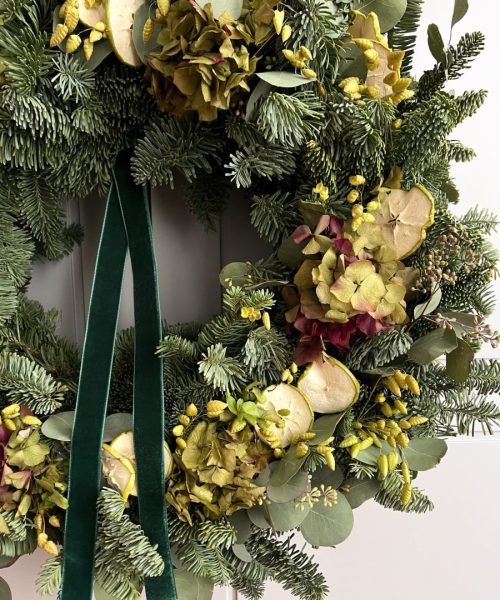 Primer plano de corona con hortensia preservada, briza seca y fruta natural