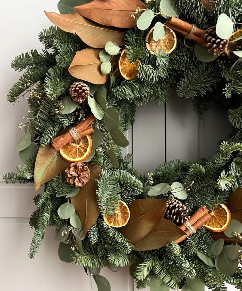 Detalle de corona navideña con canela, naranja seca y abeto natural