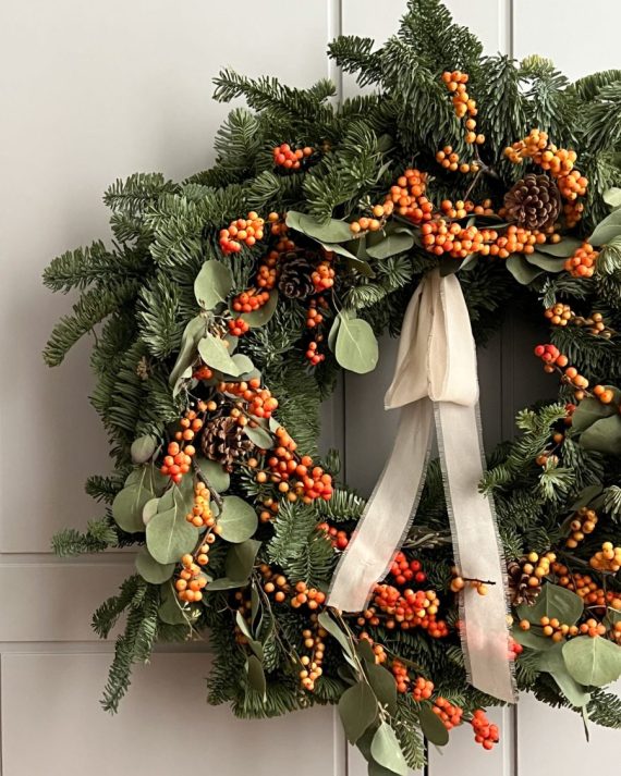 Detalle de ilex naranja y piñas naturales secas sobre abeto fresco en una corona de Navidad
